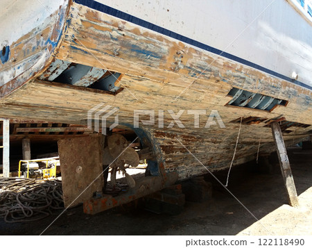 Wooden fishing boat under repair at the dock on the shores of the Red Sea in the open air. Iron ship propeller with rusty blades. The cut planks of the ship's hull and the skeleton is visible. Wooden fishing boat under repair at the dock on the shores of the Red Sea in the open air. Iron ship propeller with rusty blades. The cut planks of the ship's hull and the skeleton is visible. 122118490