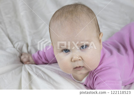 Cute and beautiful 4-month-old baby girl laying on bed and look at the camera. Infant in pink bodysuit on bed against white background. 122118523