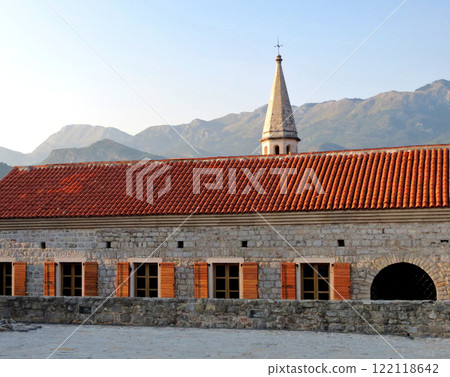 Old stone building with shuttered windows. Bell tower and mountains in the background Old stone building with shuttered windows. Bell tower and mountains in the background 122118642