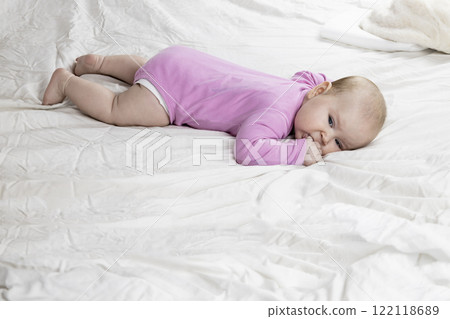 Cute and beautiful 4-month-old baby girl laying on bed. Infant in pink bodysuit on bed against white background. 122118689