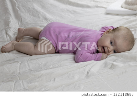 Cute and beautiful 4-month-old baby girl laying on bed. Infant in pink bodysuit on bed against white background. 122118693