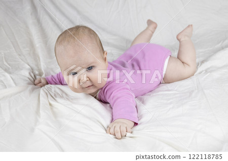Cute and beautiful 4-month-old baby girl laying on bed. Infant in pink bodysuit on bed against white background. 122118785