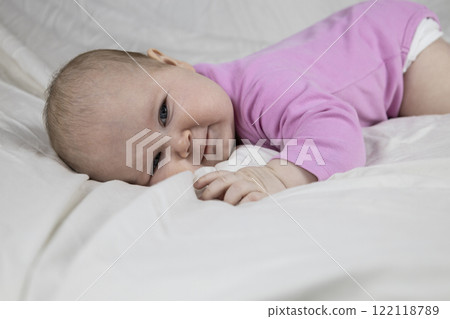 Cute and beautiful 4-month-old baby girl laying on bed and look at the camera. Infant in pink bodysuit on bed against white background. 122118789