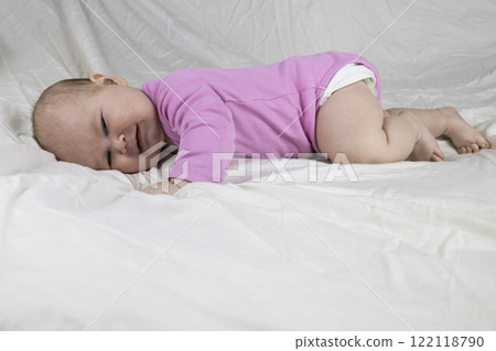 4-month-old baby girl laying on bed and crying. Infant in pink clothes wants to sleep 4-month-old baby girl laying on bed and crying. Infant in pink clothes wants to sleep 122118790