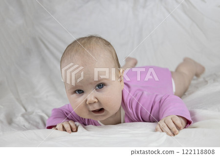 Cute and beautiful 4-month-old baby girl laying on bed and look at the camera. Infant in pink bodysuit on bed against white background. 122118808