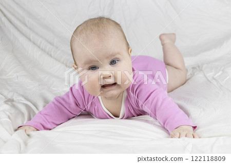 Cute and beautiful 4-month-old baby girl laying on bed and look at the camera. Infant in pink bodysuit on bed against white background. 122118809