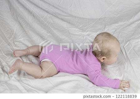 Cute and beautiful 4-month-old baby girl laying on bed. The side view of the infant in pink bodysuit on bed against white background. 122118839