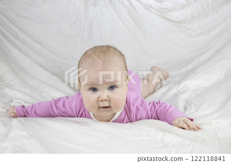 Cute and beautiful 4-month-old baby girl laying on bed and look at the camera. Infant in pink bodysuit on bed against white background. Cute and beautiful 4-month-old baby girl laying on bed and look at the camera. Infant in pink bodysuit on bed against white background. 122118841