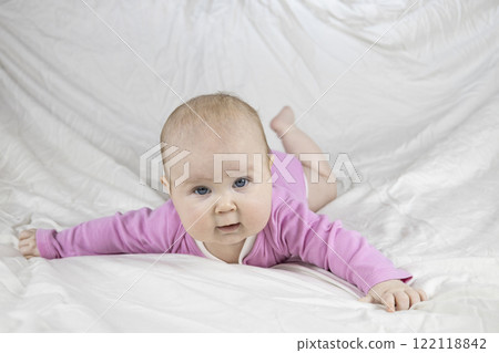 Cute and beautiful 4-month-old baby girl laying on bed and look at the camera. Infant in pink bodysuit on bed against white background. Cute and beautiful 4-month-old baby girl laying on bed and look at the camera. Infant in pink bodysuit on bed against white background. 122118842