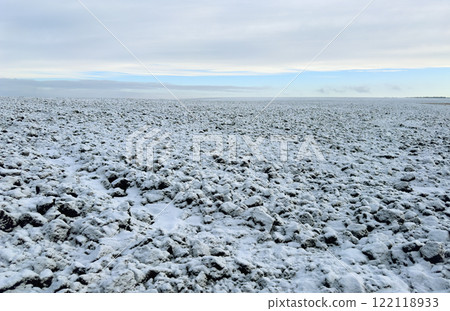 A field of black soil plowed for the winter, covered with snow against the background of a blue winter sky 122118933