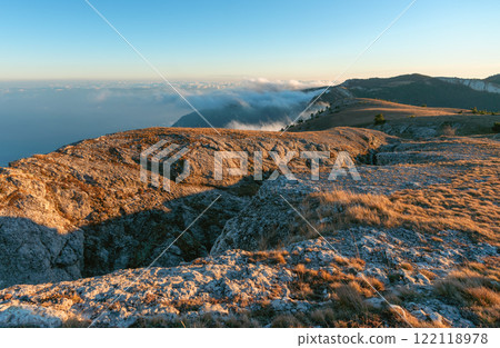 A mountain crevice illuminated by the evening sun located above the clouds 122118978