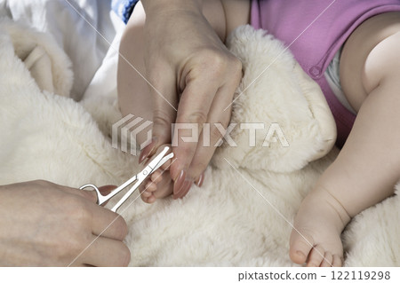 Mom trims baby's nails with baby scissors. Close up photo of mother's hands holding feet of the infant and nail scissors. 122119298