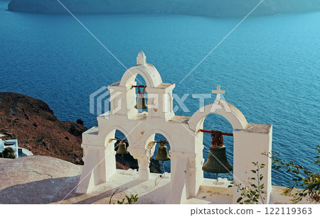 Ancient bell tower with old bells of a Christian church against the background of the blue sea. Ancient bell tower with old bells of a Christian church against the background of the blue sea. 122119363