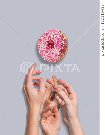 Several hands reach for a levitating glazed pink donut on blue background. Several hands reach for a levitating glazed pink donut on blue background. 122119455