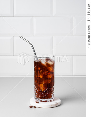Cold brew coffee in a glass with ice and straw on a light table against a white brick background Cold brew coffee in a glass with ice and straw on a light table against a white brick background 122119456