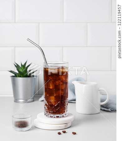 Cold brew coffee in a glass with ice and straw on a light table against a white brick background Cold brew coffee in a glass with ice and straw on a light table against a white brick background 122119457