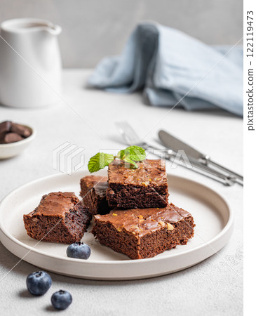Chocolate brownie with nuts cut into pieces on a plate with blueberry and mint on a light background 122119473