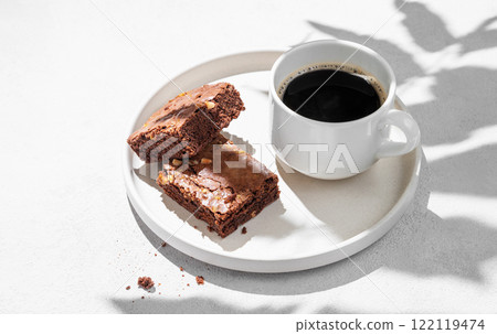 Pieces of chocolate brownie with nuts on a plate with a cup of espresso coffee on a light background 122119474