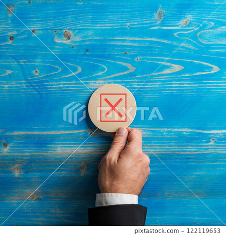 Hand of a businessman placing a wooden cut  circle with a red x sign on it over blue background 122119653