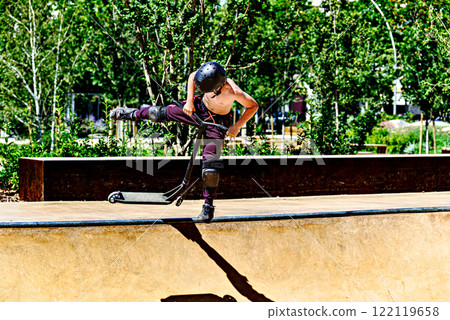 Young man practicing Scootering (Freestyle Scootering) in the new SkatePark of the central park of Igualada, Barcelona, Spain 122119658