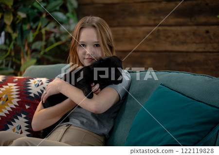 A warm and cozy indoor scene featuring a playful child and their adorable black puppy 122119828