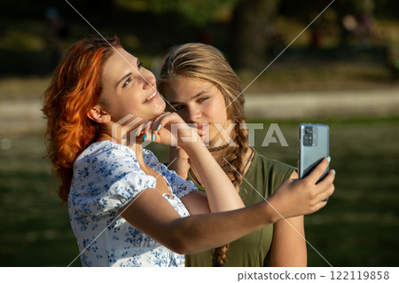 Two close friends joyfully taking a fun selfie together in a beautiful park setting 122119858