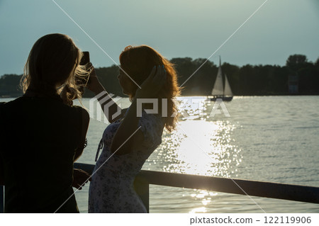 A beautiful silhouette of friends enjoying a stunning sunset by the tranquil waters edge 122119906