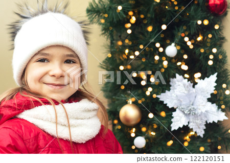 The girl stands near the Christmas tree with a bright garland. New Year card. 122120151