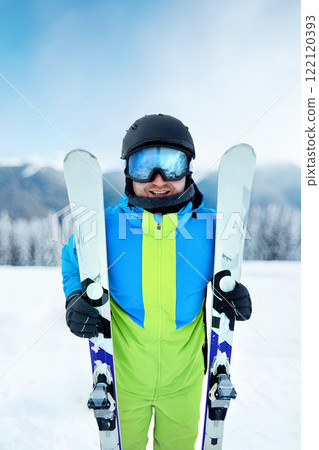 Portrait of a skier in the ski resort on the background of mountains and blue sky. Ski goggles of a man wearing ski glasses. Winter Sports 122120393