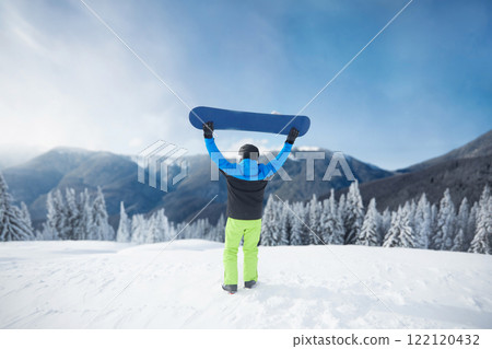 Snowboarder Of Man At Ski Resort On Blue Sky and Snow Mountains Background, Hold Snowboard. Winter Sports 122120432