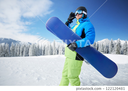 Portrait of man at ski resort on the background mountains holds snowboard. Wearing ski glasses Portrait of man at ski resort on the background mountains holds snowboard. Wearing ski glasses 122120481