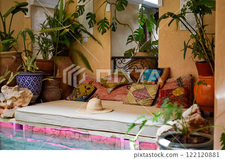 Balinese Bed with colorful cushions, decorative plants, a hat and swimming pool 122120881