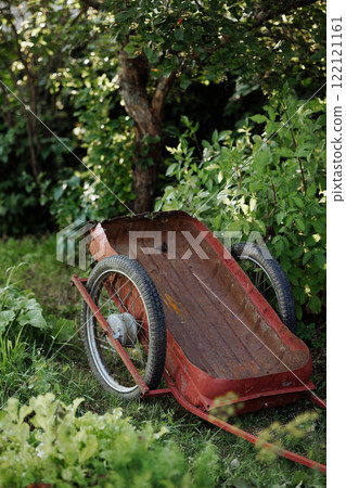An old red wheelbarrow stands near an old wooden fence. An old red wheelbarrow stands near an old wooden fence. 122121161