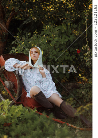 A fashionable woman poses on a red wheelbarrow in the garden 122121162
