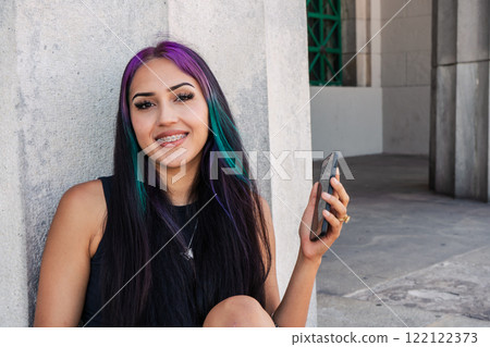 A young woman sitting with her cell phone on a staircase landing 122122373