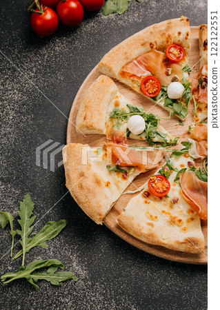 Delectable slices of gourmet pizza with prosciutto, arugula, mozzarella, and cherry tomatoes Delectable slices of gourmet pizza with prosciutto, arugula, mozzarella, and cherry tomatoes 122122551