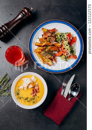 Gourmet business lunch with potatoes, vegetable salad, and creamy soup with bacon and croutons 122122578