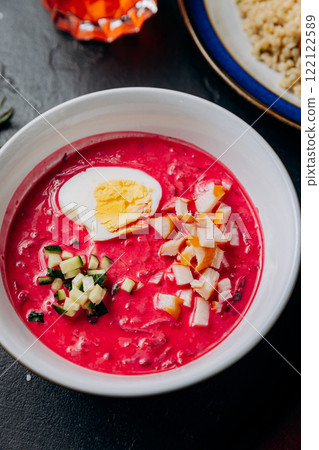 Vibrant beetroot soup with boiled egg, smoked chicken, and cucumber in a white bowl 122122589