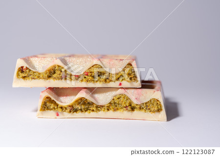 Trend white Dubai chocolate with pistachio, dried raspberry, tahini and kadaif, on white background, isolated, showing the filling. Confectionery and handmade sweets, chocolatier 122123087