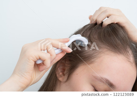 Close up of young woman using microneedling derma roller on head for stimulating new hair growth, copy space for text. Alopecia treatment, scalp stimulation, hair loss and baldness targeted therapy. Close up of young woman using microneedling derma roller on head for stimulating new hair growth, copy space for text. Alopecia treatment, scalp stimulation, hair loss and baldness targeted therapy. 122123089
