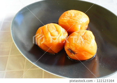 三個美味的醃李子放在盤子裡。茨城縣水戶市的土特產。 三個美味的醃李子放在盤子裡。茨城縣水戶市的土特產。 122123164