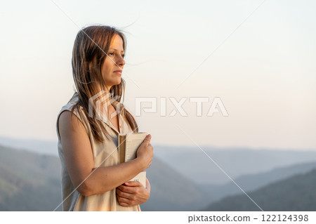 Woman with a book in mountain landscape during golden hour, showing tranquility and contemplation 122124398