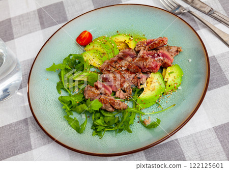 Grilled beef steak with seasonings, served with avocado, sesame seeds and parsley, tomatoes 122125601