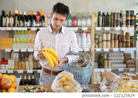 Near counter, man client takes out bananas from pile of fruits, chooses ripe fruits Near counter, man client takes out bananas from pile of fruits, chooses ripe fruits 122125624