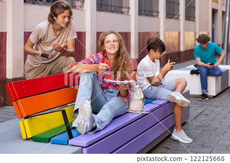 Schoolchildren sitting on bench in schoolyard 122125668
