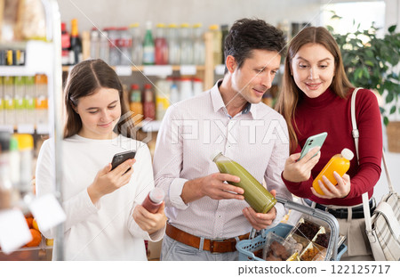 Family with teenage girl scanning QR on bottle of smoothie in supermarket Family with teenage girl scanning QR on bottle of smoothie in supermarket 122125717
