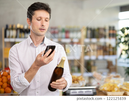 Man in light shirt scan QR code and take reading beer label using phone camera in shop 122125839