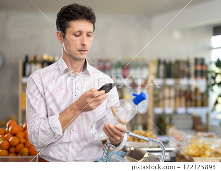 Man in light shirt scan QR code and take reading soda water label using phone camera in shop 122125893