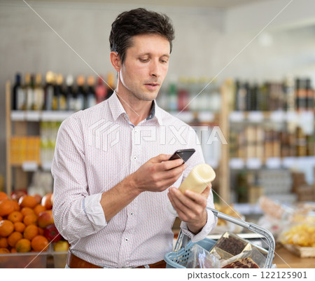 Man in light shirt scan QR code and take reading mayonnaise label using phone camera in shop 122125901