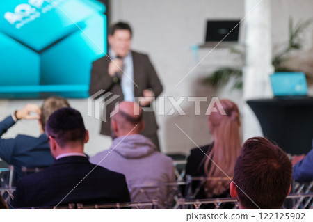 Business conference presentation with speaker addressing engaged audience and digital screens Business conference presentation with speaker addressing engaged audience and digital screens 122125902